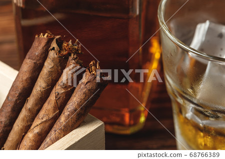 Glass of whiskey and rolled cigars on wooden table Glass of whiskey and rolled cigars on wooden table 68766389