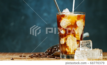 Pouring milk in iced coffee on grey background Pouring milk in iced coffee on grey background 68770379