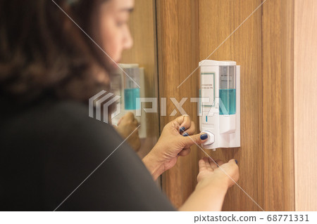 Woman washing hand with alcohol gel after using public elevator. 68771331