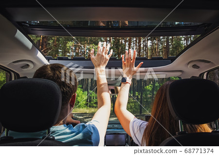 Couple in the car with their hands through open hatch travelling on the road through trees Couple in the car with their hands through open hatch travelling on the road through trees 68771374