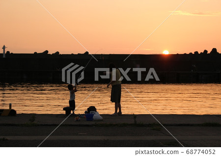 Mother with children fishing on embankment in the harbor at sunset 68774052