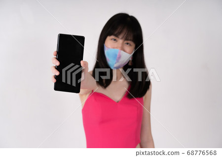 Asian woman wearing protective mask holding phone 68776568