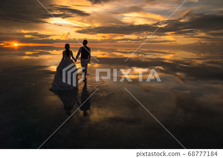 Bride and groom heading for the sunset in the mirror of the sky 68777184