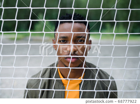 Frustrated young black man behind net outdoors in city, black lives matter concept. Frustrated young black man behind net outdoors in city, black lives matter concept. 68777922