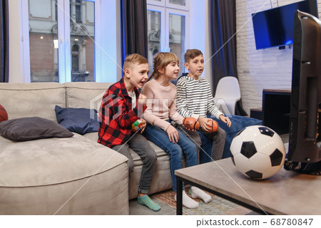 Funny three child friends are sitting on the couch at home and enjoying soccer match and shouting when see scored ball. 68780847