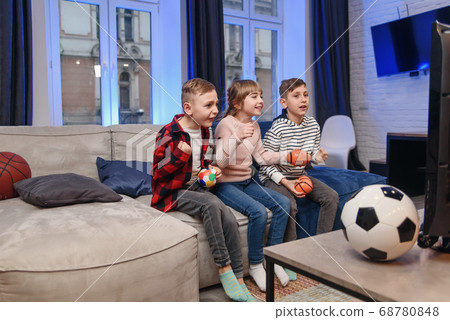 Funny three child friends are sitting on the couch at home and enjoying soccer match and shouting when see scored ball. 68780848