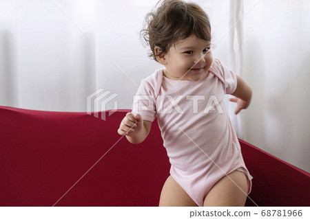 Little cute baby girl play on red sofa at home. 68781966