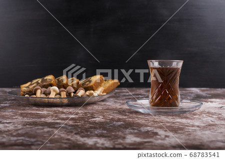 Sliced cocoa pie with cookies in a glass platter with a glass of tea on black background 68783541