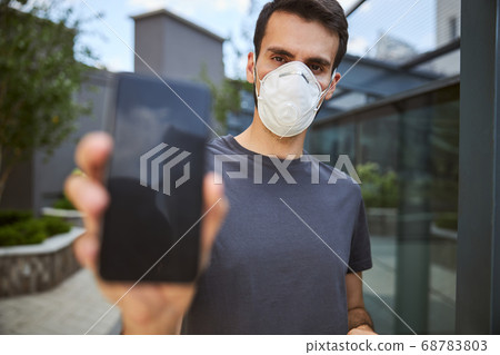 Serious man in a t-shirt demonstrating his gadget Serious man in a t-shirt demonstrating his gadget 68783803