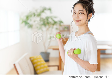 Young woman doing strength training with dumbbells in the room Young woman doing strength training with dumbbells in the room 68784912