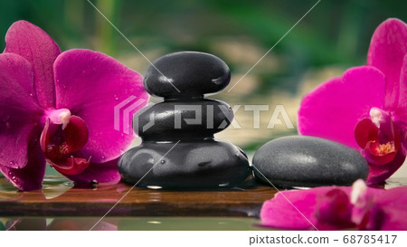 Black zen stones and pink orchids on a wooden plank on the surface of the water. SPA, relaxation, meditation concept Black zen stones and pink orchids on a wooden plank on the surface of the water. SPA, relaxation, meditation concept 68785417