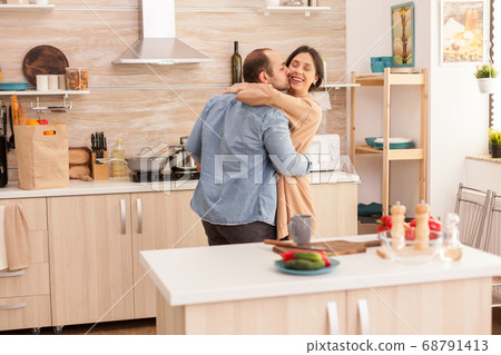 Man kissing wife in kitchen Man kissing wife in kitchen 68791413