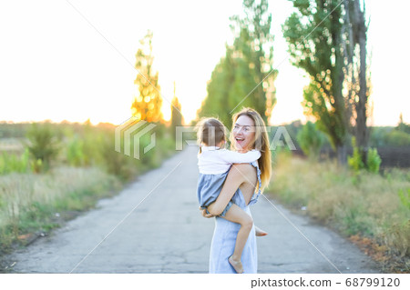 Blonde young american mother holding female kid on road. Blonde young american mother holding female kid on road. 68799120