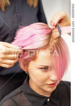 Hairdresser straights pink hair of woman by hair 68800402
