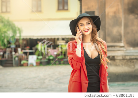 Woman is talking by phone in city street outdoors Woman is talking by phone in city street outdoors 68801195