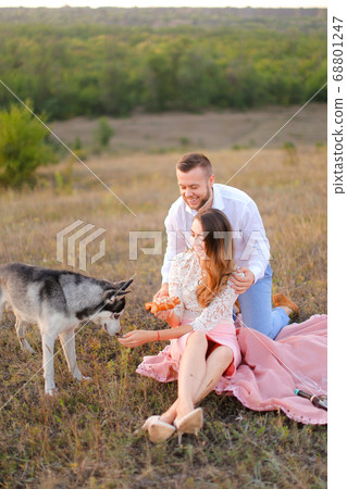 Young happy girl and boy sitting on pink plaid near husky and resting. Young happy girl and boy sitting on pink plaid near husky and resting. 68801247