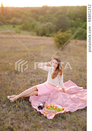 Young happy girl sitting on pink plaid near bottle of wine and fruits. Young happy girl sitting on pink plaid near bottle of wine and fruits. 68801252