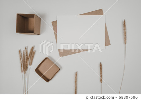 Blank white paper on brown paper envelope with Bristly foxtail dry flower and Carton box. Mock-up of horizontal blank greeting card. Top view of Craft  envelope on white background. Flat lay minimalis 68807590