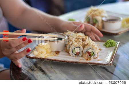 Woman eating sushi set with soy sauce, wasabi and sticks in restaurant Woman eating sushi set with soy sauce, wasabi and sticks in restaurant 68807966