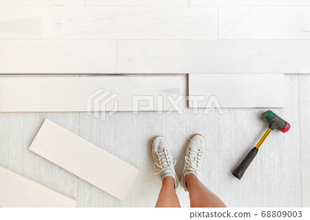 Home improvement floor installation - Worker installing new hardwood flooring at house or condo .Engineered wood floor planks of natural white maple wood. Flooring glued or floating over membrane Home improvement floor installation - Worker installing new hardwood flooring at house or condo .Engineered wood floor planks of natural white maple wood. Flooring glued or floating over membrane 68809003