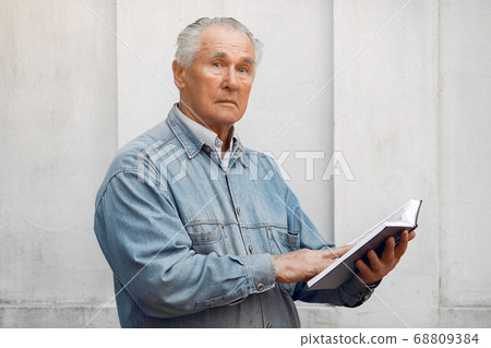 Elegant old man standing on gray background with a book Elegant old man standing on gray background with a book 68809384