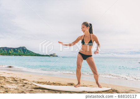 Asian tourist woman on Hawaii beach learning to surf at surfing school in Waikiki, Honolulu, Oahu. Girl having fun practicing on surfboard on shore Asian tourist woman on Hawaii beach learning to surf at surfing school in Waikiki, Honolulu, Oahu. Girl having fun practicing on surfboard on shore 68810117