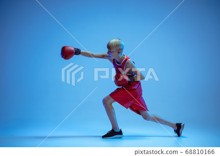 Teenager in sportswear boxing isolated on blue studio background in neon light 68810166