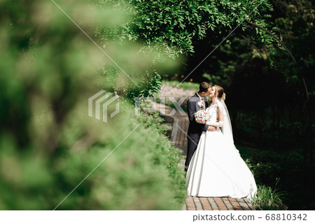 Beautiful bride and groom embracing and kissing on their wedding day outdoors Beautiful bride and groom embracing and kissing on their wedding day outdoors 68810342