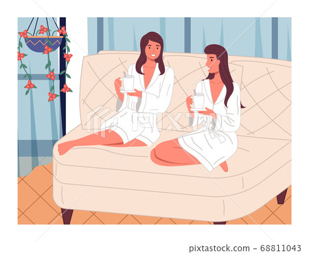 Two beautiful girls in terry white bathrobes on the couch with cups of drink. Spa treatments 68811043