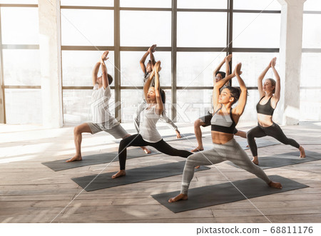 Group Of Young Yoga Enthusiasts Training Together In Studio, Practicing Warrior Pose 68811176