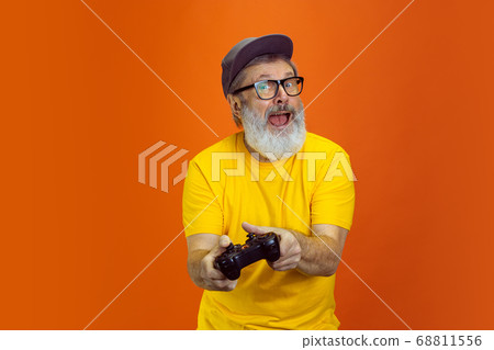 Senior hipster man using devices, gadgets on orange background. Tech and joyful elderly lifestyle concept Senior hipster man using devices, gadgets on orange background. Tech and joyful elderly lifestyle concept 68811556