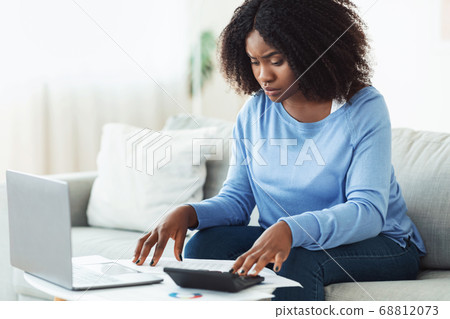 Woman using calculator and laptop at home 68812073