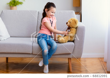 Asian kid girl playing doctor treating bear toy at home Asian kid girl playing doctor treating bear toy at home 68812091