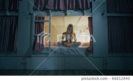 Young attractive woman sitting on the bed in the hostel room and using smartphone at night 68812840