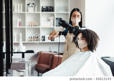 Young hairdresser in protective mask making stylish hairdo for customer 68813243