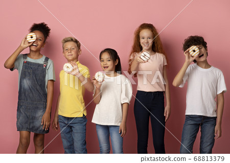 Joyful multiethnic schoolkids with tasty donuts over pink background Joyful multiethnic schoolkids with tasty donuts over pink background 68813379