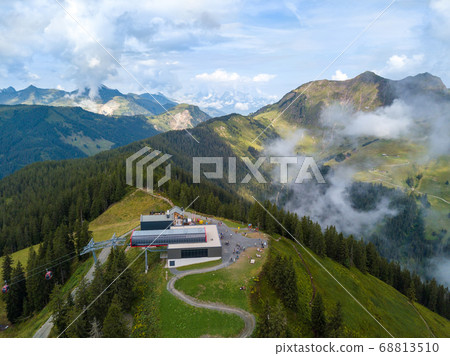 Aerial view on Kohlmais mountain station in Saalbach Austria as starting point for mountainbike trails and hikers in summer with great mountain panorama in the clouds Aerial view on Kohlmais mountain station in Saalbach Austria as starting point for mountainbike trails and hikers in summer with great mountain panorama in the clouds 68813510