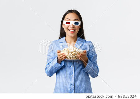 Home leisure, sleepover and slumber party concept. Enthusiastic asian girl in pajamas and 3d glasses, holding bowl of popcorn and smiling amused as watching premier on tv, enjoying movie night Home leisure, sleepover and slumber party concept. Enthusiastic asian girl in pajamas and 3d glasses, holding bowl of popcorn and smiling amused as watching premier on tv, enjoying movie night 68815024