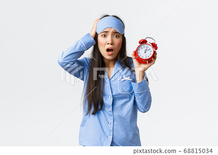 Woman having panic as showing alarm, being late for work, overslept to morning exam, holding hand on head and frowning nervous, standing in blue pajamas and sleeping mask anxious 68815034