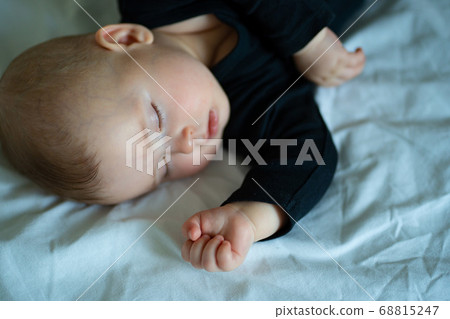 kid in black clothes is sleeping on a white bed 68815247