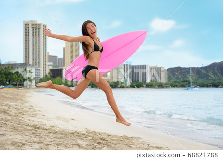 Surfing summer fun woman jumping of joy on beach with surfboard. Surf vacation lifestyle. Asian girl in bikini, sport and fitness active concept. 68821788