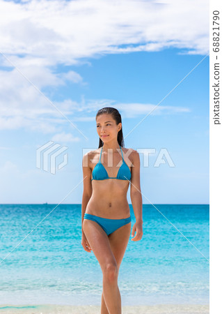 Beach vacation bikini body Asian woman walking relaxing on paradise tropical vacation with fit toned stomach and slim legs. Sexy Chinese multiracial model in blue swimsuit coming out of ocean water. 68821790