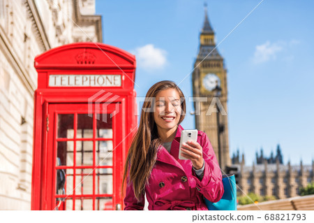 London mobile phone businesswoman walking in the city in stylish pink trench coat, urban lifestyle. Red telephone booth and Big Ben background London, England, UK. Europe travel. London mobile phone businesswoman walking in the city in stylish pink trench coat, urban lifestyle. Red telephone booth and Big Ben background London, England, UK. Europe travel. 68821793