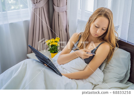 Woman lies in bed and has an online consultation with doctor GP 68833258