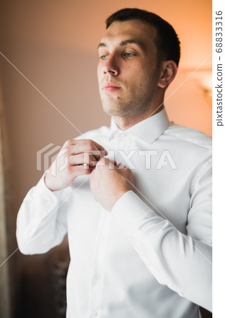 Grooms morning preparation. Handsome man getting dressed and preparing for the wedding Grooms morning preparation. Handsome man getting dressed and preparing for the wedding 68833316