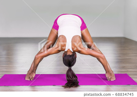Yoga girl doing wide leg forward fold at gym. Woman stretching legs muscles doing Prasarita Padottanasana training stretches on exercise mat in fitness class. 68834745