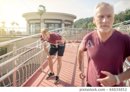 Grey-haired male running across bridge, young male holding hand on his chest behind him Grey-haired male running across bridge, young male holding hand on his chest behind him 68839852