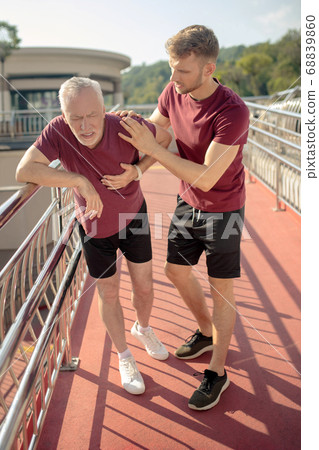 Mature grey-haired male holding his hand on chest, young male helping him 68839860