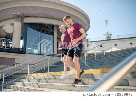 Young bearded male and mature grey-haired male running down stairs 68839972