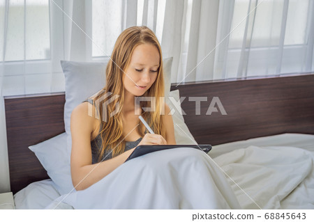 Woman draws on tablet with stylus in bed 68845643